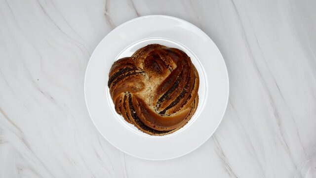 Poppy Seed Bun On White Plate Rotating On Marble Background. Top View.