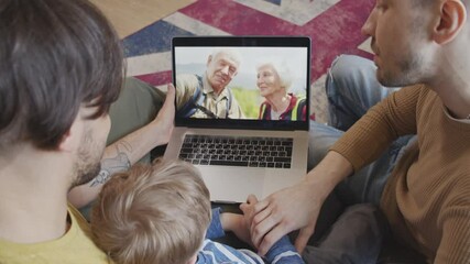 Over the shoulder shot of same-sex male couple and their little son using laptop and talking on video call with elderly man and woman - Powered by Adobe