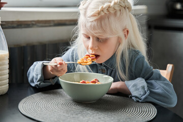 Girl eating corn flakes with milk to the breakfast while sitting at the kitchen