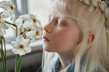 Naklejka premium Girl standing at the table and smells flowers at the vase