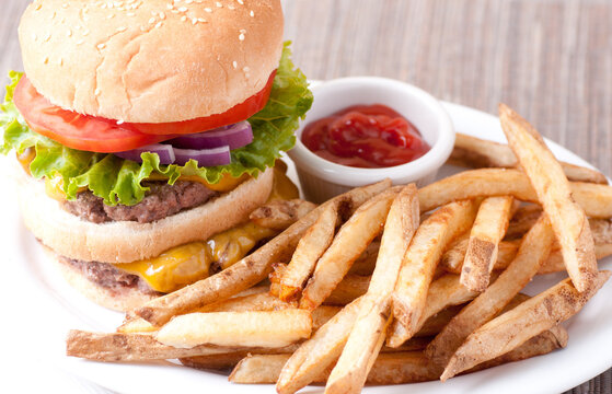 Closeup shot of a cheeseburger with fresh french fries and tomato on a white plate