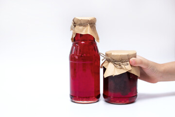 The hand holds another one, to Jars of different shapes with strawberry syrup and jam on a white background.