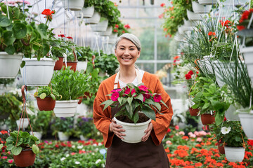 Senior woman posing to the camera with plants at the pot and smiling toothy
