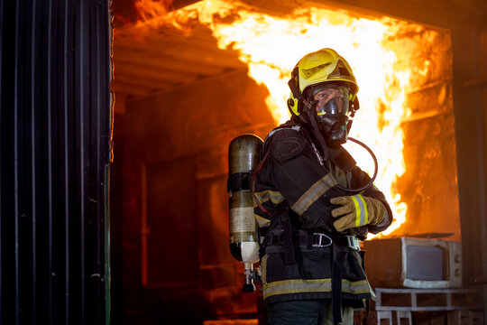Firefighter man with protective and safety clothes stand with arm-crossed in front of fire on wall and ceiling in the kitchen.