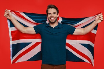 Handsome young man in casual wear carrying British flag and smiling