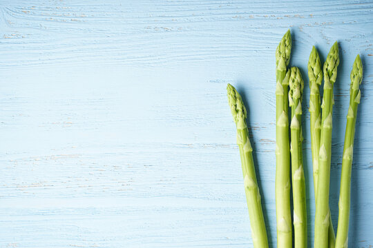 Fresh green asparagus on blue wooden background, close-up. Flat lay.