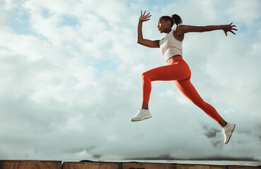 Female athlete in sportswear lunging and jumping midair - obrazy, fototapety, plakaty