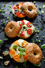 Grilled bagel sandwiches with with cherry tomatoes, olives, mozzarella cheese and herbs  on a dark...
