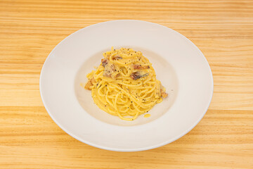 Italian recipe of spaghetti carbonara with guanciale on white plate and light wooden table