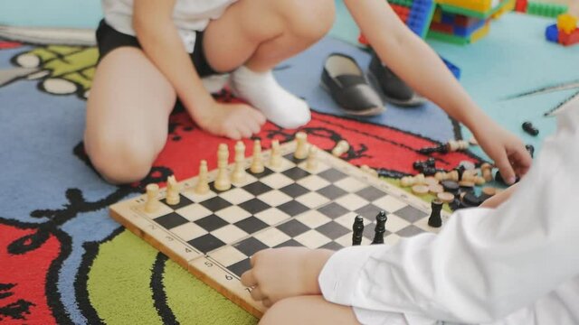 children teenagers play chess in kindergarten sitting on the floor. Close-up.