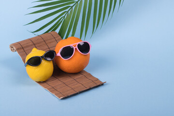 Orange and lemon fruit hipster in sunglasses lying on sun bed on pastel blue background.