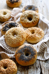 Bagels made using traditional methods with the addition of various seeds on a rustic wooden table, focus on the bagel with poppy seeds, close up view