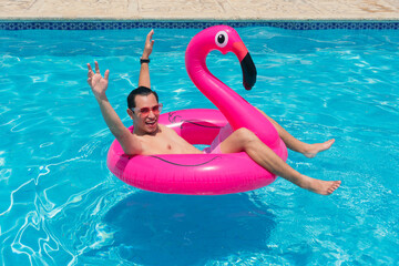 A man has fun on a fuchsia flamingo inflatable float in the pool.