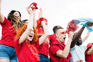 Excited group of multiracial friends watching soccer match event - Red sport fans screaming while...