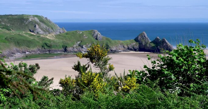 Elevated 4K view of Three Cliffs Bay in the Gower, a stunning sandy cove on the coast of Wales. Three large rocks stand along on the eastern edge of this popular tourist hotspot in The Gower Peninsula