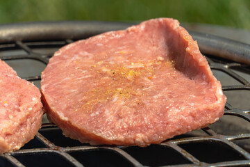 Photo of a turkey burger cooking above a fire pit on a sunny day of June 20, 2021. Below the grill surface, the fire consists mainly of mesquite dried-wood logs and fruit wood charcoal.