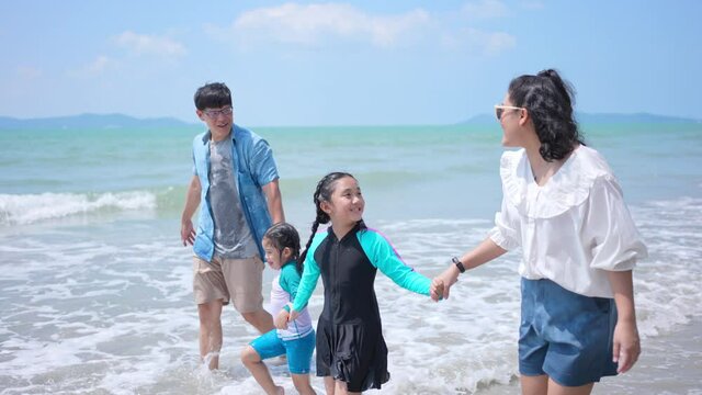 Asian family on summer vacation. Parents with two child girl kid walking on the beach with playing sea water together. Two sisters sibling having fun outdoor lifestyle activity with father and mother.
