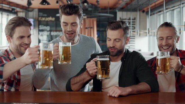 Happy young men in casual clothing toasting each other with beer the pub