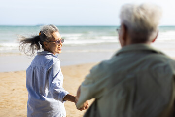 Retired couple holding hand happily walked down to the sandy beach.An elderly wife holding her husband's hand and smile happily. Plan life insurance and retirement concept.