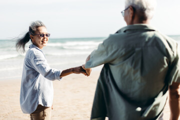 Retired couple holding hand happily walked down to the sandy beach.An elderly wife holding her...
