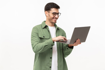 Young man wearing casual green shirt, standing with opened laptop in hands, surfing online,...