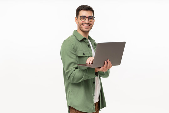 Portrait of young modern businessman standing holding laptop and looking at camera with happy smile, isolated on gray
