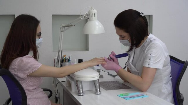 Young woman with glasses in a manicure salon. A manicurist uses a drill machine to remove nails.