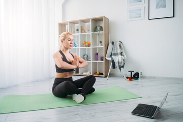 Online yoga. Meditating woman. Home practice. Mental health. Inspired lady black sportswear sitting lotus pose namaste hands looking laptop in light room interior.