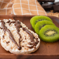 Rice crackers with peanut butter and chocolate-flavored cocoa, accompanied by kiwi slices