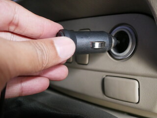 hand holding plug 12 volt into socket from car cigarette lighter.
