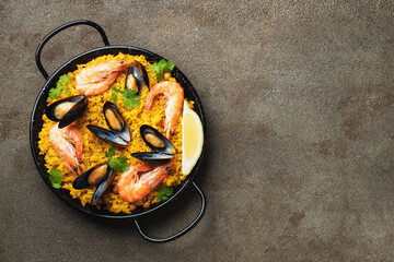 Traditional spanish seafood paella in pan with chickpeas, shrimps, mussels, squid on brown concrete background. Top view with copy space