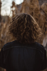 Back view of teenage boy with long curly brown hair wearing a jean jacket