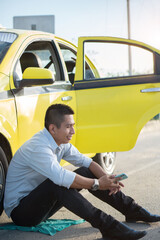 Latino man sitting next to a yellow vehicle while checking the cell phone. Cabbie. Hispanic taxi...