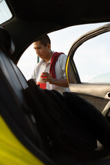 Latino man with a flannel on his shoulder and holding orange traffic cones, outside his vehicle. Brunette taxi driver, guarding orange traffic cones.