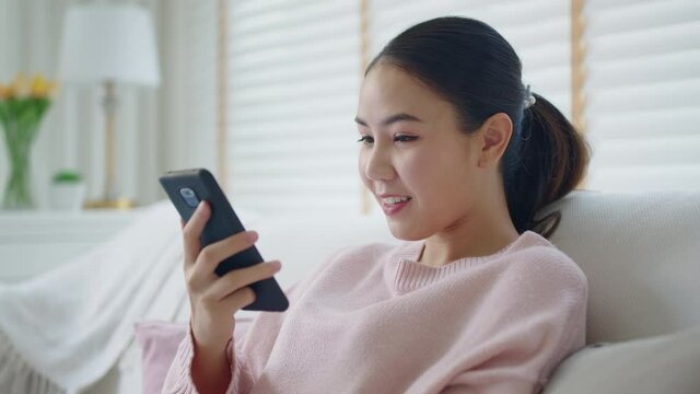 Asia young people teen happy girl sit relax call use smart phone talk chat send text to 5G wifi mic VoIP deep tech ai bot app at home sofa couch. Enjoy vocal order to help chatbot iot on social media.