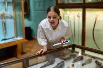 Young girl in the museum looks at the exposition behind a glass case