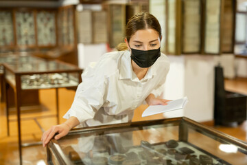 Fototapeta na wymiar Woman in protective mask looking at exhibits in glazed stands in historical museum