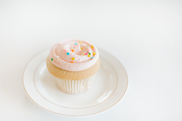 Decorated vanilla cupcake with pink frosting and rainbow sugar sprinkles on a plate
