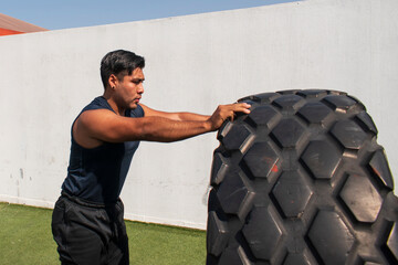 latin or native american man lifting up a tire while he´s doing crossfit outside of his gym in a sunny day