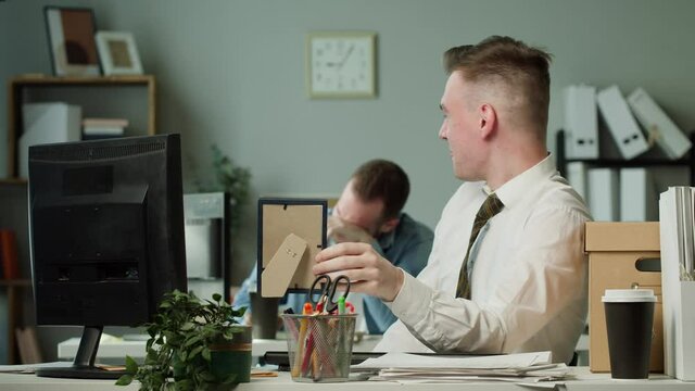 Businessman sitting and showing photo to his partner, laughing together in office, smiling man stops working, having break during paperwork, end of working day. Casually dressed workers having fun. 