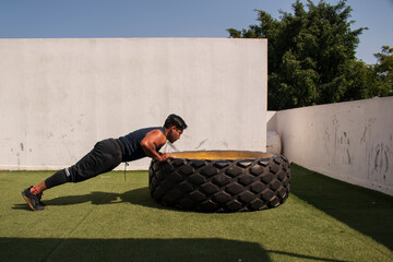 latin or native american men doing push ups in a tire outdoors in front of his gym in a sunny day
