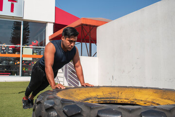 latin or native american men doing push ups in a tire outdoors in front of his gym in a sunny day