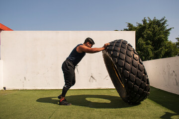 latin or native american man lifting up a tire while he´s doing crossfit outside of his gym in a sunny day