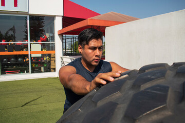 latin or native american man lifting up a tire while he´s doing crossfit outside of his gym in a sunny day