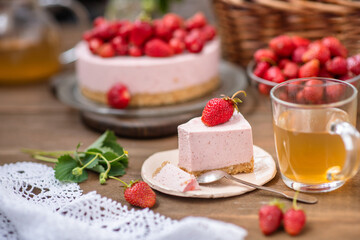 A piece of cheesecake lying on a plate next to a cup of sea buckthorn tea on the background of a whole cake