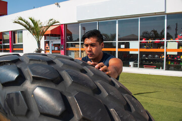 latin or native american man lifting up a tire while he´s doing crossfit outside of his gym in a sunny day