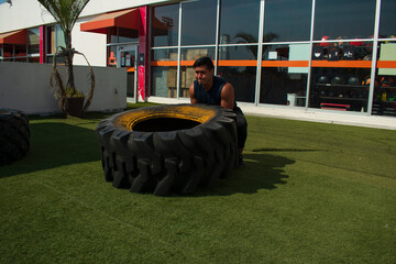 latin or native american man lifting up a tire while he´s doing crossfit outside of his gym in a sunny day
