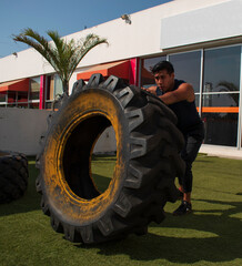 latin or native american man lifting up a tire while he´s doing crossfit outside of his gym in a sunny day