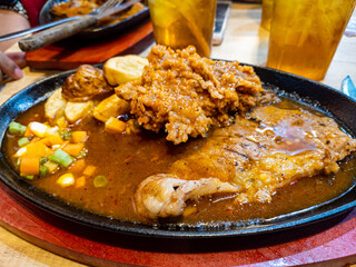 Close up thin grilled sirloin beef steak on a hot plate with fried chicken, potato, vegetables and black pepper sauce at indonesian restaurant.