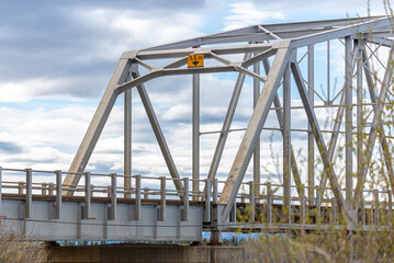 Naklejka premium Large man made structure steel bridge spanning across Nisutlin Bay in township of Teslin flowing to the Yukon River in northern Canada during spring summer time with cloudy blue sky background.